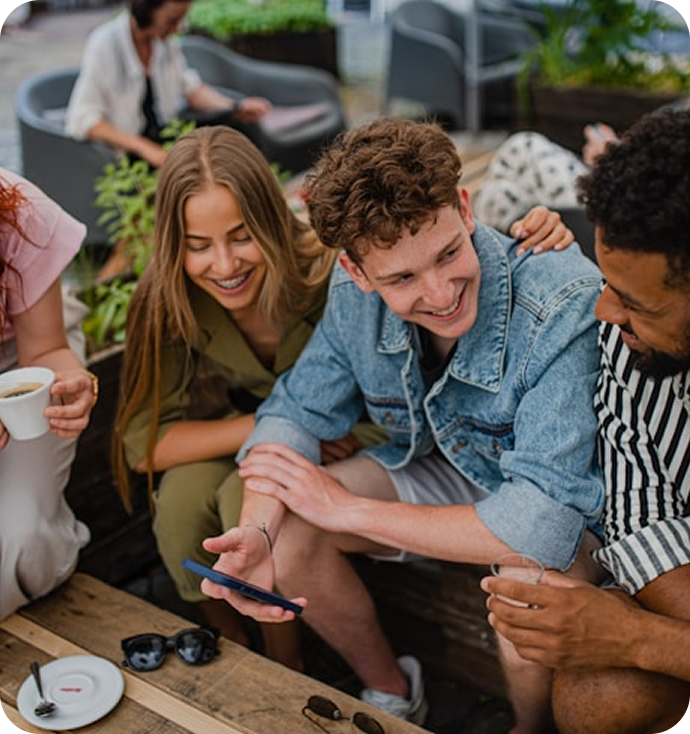 A small group of friends gathered around a table looking at a phone
